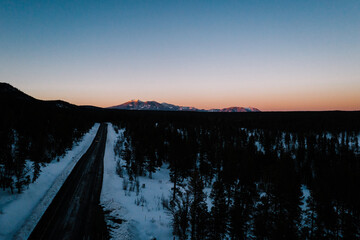 aerial view of a sunset over the mountains and snowy forest