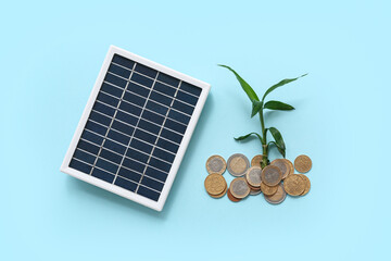 Portable solar panel with plant and coins on blue background. Green Energy concept