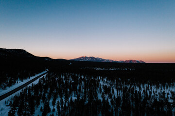 aerial view of a sunset over the mountains and snowy forest