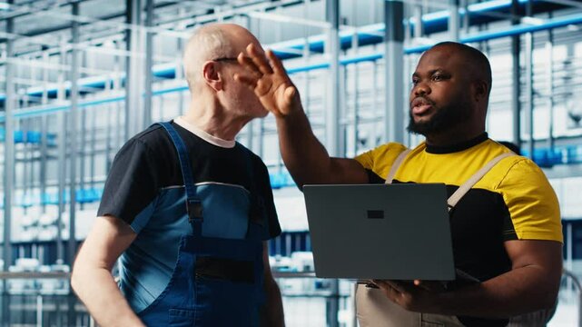Smart factory senior engineer teaching new trainee to manage robotic arms. Industry 4.0 industrial plant team leader and intern controlling automated machinery, ensuring workflow continuity, camera A