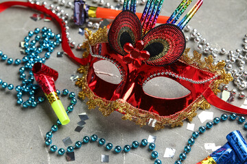Beautiful red carnival mask with party horns, confetti and decor on grey background. Closeup