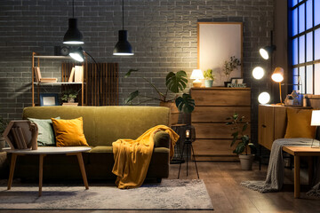 Sofa, coffee table with wooden hand, books and glowing lamps in interior of living room