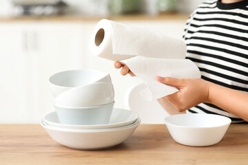 Beautiful young woman with clean plates and roll of paper towels in kitchen, closeup