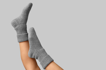 Legs of young woman in warm knitted socks on grey background