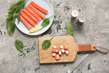 Wooden board and plate with tasty crab sticks on grey background © Pixel-Shot