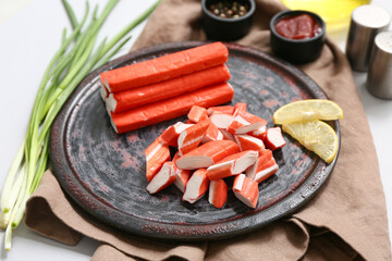 Plate with tasty crab sticks, slices of lemon and green onion on grey background © Pixel-Shot