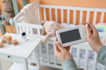 Woman holding baby monitor near crib in children's bedroom, closeup