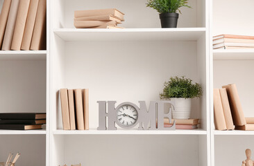 Shelves with books, clock and stylish decor, closeup