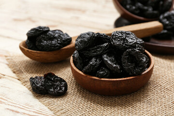 Bowl and spoon with dried prunes on white wooden background