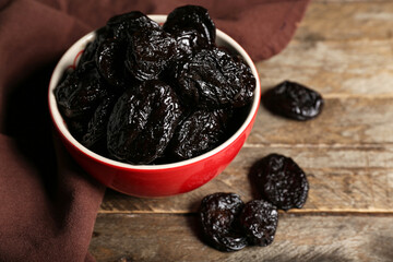 Bowl with dried prunes on wooden background