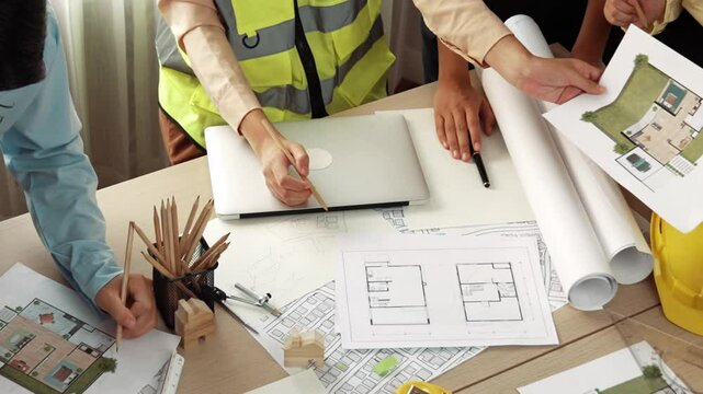 Smart architect and safety engineer discussion about building blueprint on table with architectural document, measurement tools and wooden block scatter around at modern office. Closeup. Delineation.
