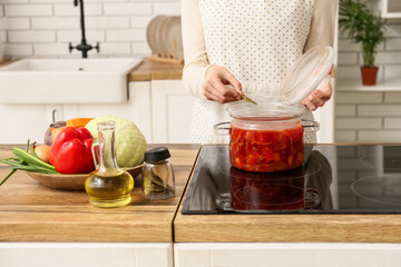 Young woman adding bay leaves to pot with delicious borscht in kitchen, closeup