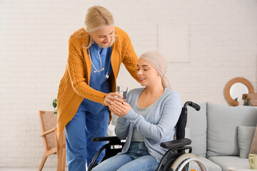 Young woman after chemotherapy in wheelchair taking glass of water from nurse at home. Brain cancer...