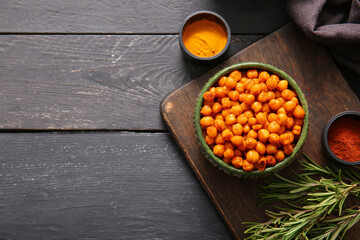 Bowl with tasty fried chickpeas, rosemary and spices on black wooden background