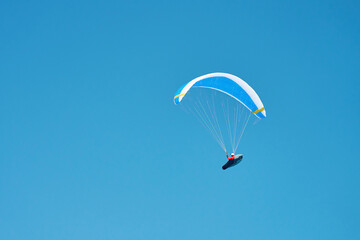 Person is flying on paraglider against clear sky. Paraglide with blue canopy. Extremal sport