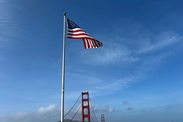American flag waving in the breeze near Golden Gate Bridge under clear blue sky