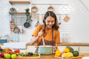 Young woman standing near stove and cooking, housewife, meal, chef, food.Happy woman looking and smelling tasting fresh delicious from soup in a pot with steam at white interior kitchen