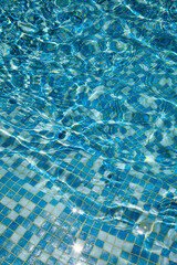 Crystal-clear water rippling over blue mosaic tiles in swimming pool