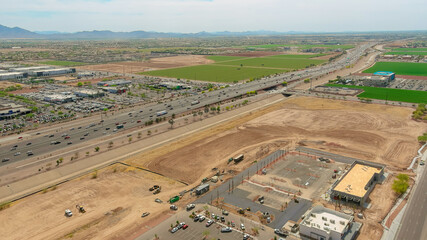 Aerial view shows busy highway near fields, construction, showcasing urban growth in desert near Phoenix Arizona