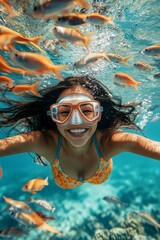 Fototapeta premium Serene ocean escape. A dense school of silver fish swims next to her. A lovely and sexy happy mixed-race young woman with black hair in a swimming mask and fins snorkeling among the corals.