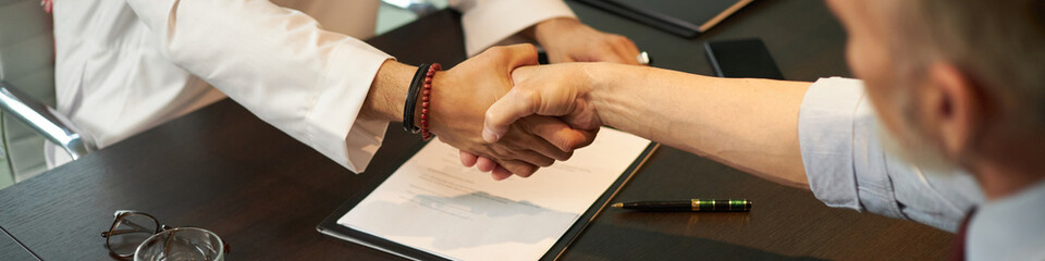 High angle view of two ethnically diverse businessmen doing handshake after signing agreement,...