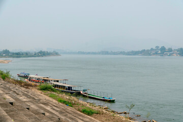 Chiang Saen, Thailand - April 30, 2024: Boats sit near the bank of the Mekong River with Laos in the background, smog