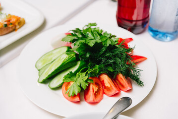 Fresh Vegetable Plate with Tomatoes, Cucumbers, and Herbs. Healthy sliced cucumbers and tomatoes served with fresh parsley and dill on a white plate, perfect as a salad or appetizer.