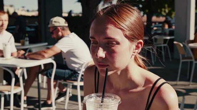 Young woman enjoys iced beverage at outdoor cafe on sunny day