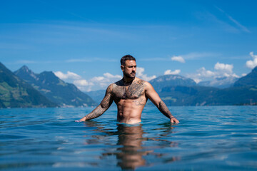 Fototapeta premium Sexy summer man. Wet muscular male body in water. Nude sexy male body. Man splash in water in summer nature. Fit man posing by summer beach. Strong man splashing in a mountain lake. Summer trip.