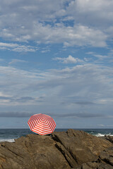 Red and white umbrella on a rocky headland