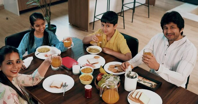 Indian Asian young family of four, including loving parents, son, a daughter, joyfully having breakfast together at a dining table in a beautifully designed modern home, enjoying a healthy meal