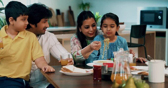Indian Asian young family of four, including loving parents, son, a daughter, joyfully having breakfast together at a dining table in a beautifully designed modern home, enjoying a healthy meal
