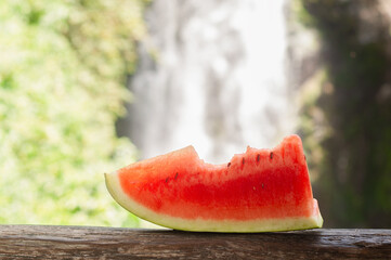 A Refreshing Slice of Juicy Watermelon Set Against a Beautifully Serene Waterfall Backdrop