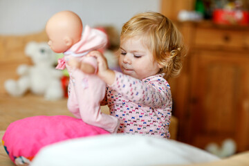 Adorable cute little toddler girl playing with doll. Happy healthy baby child having fun with role...
