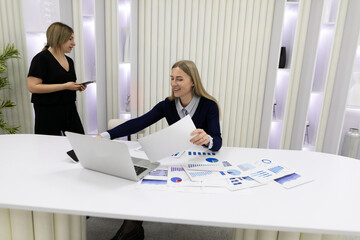 Business meeting in an office with two women analyzing reports and discussing projections in a modern workspace
