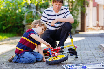 Little kid boy and father repair chain on bikes and change wheel of balance bicycle. Family work...