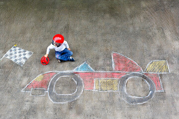 Happy healthy little boy having fun with racing car picture drawing with chalk. Creative leisure...