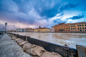 Dramatic view of the swollen Arno River at sunset with flood defenses along Pisa’s Lungarni