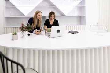 Two women collaborate at a modern workspace while discussing ideas on a laptop