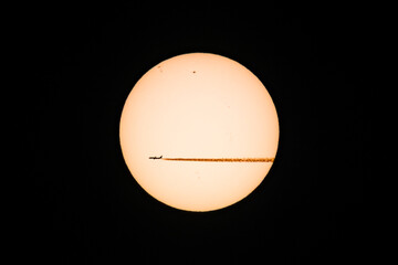 A jet plane and its vapour trail silhouetted as it passes the sun