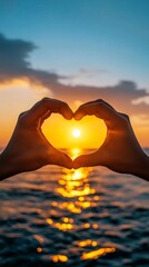 Hands making heart shape framing golden sunset over ocean with bokeh effect