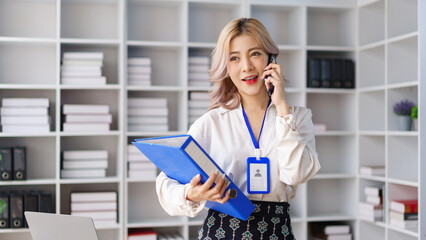 Professional businesswoman talking on smartphone while holding project folders in modern office