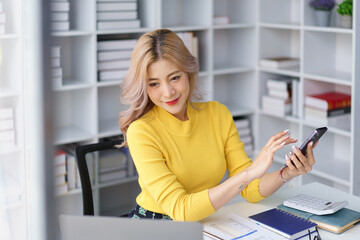 Smiling businesswoman using smartphone during break at office desk with laptop and notebook