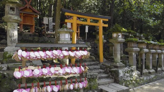 Heart shaped ema prayer tags hang beside torii gate at shrine in Nara, Japan, tilt up along entrance pathway