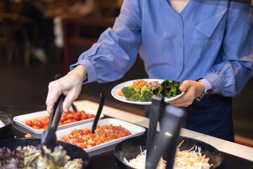 Close-up of a woman choosing vegetables at a salad bar