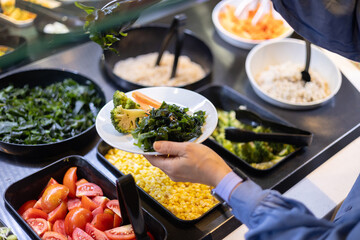 Close-up of a woman choosing vegetables at a salad bar