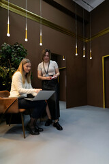 Fototapeta premium Two women collaborate at a modern workspace with warm lighting and stylish decor