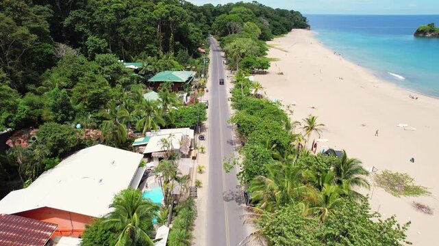 A cinematic overhead shot of a road of travelers and tourists driving down the beach Playa Cocles revealing the popular tourist destination Puerto Viejo on the Caribbean coast of Costa Rica.