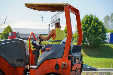 Close-up of construction worker operating vibration compact roller on highway construction site