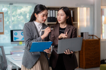 Two Businesswomen Discussing Work Using Laptop and Clipboard in Office